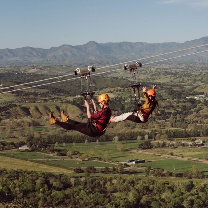 Two guests on the dual ziplines flying toward the camera above the Santa Ynez Valley