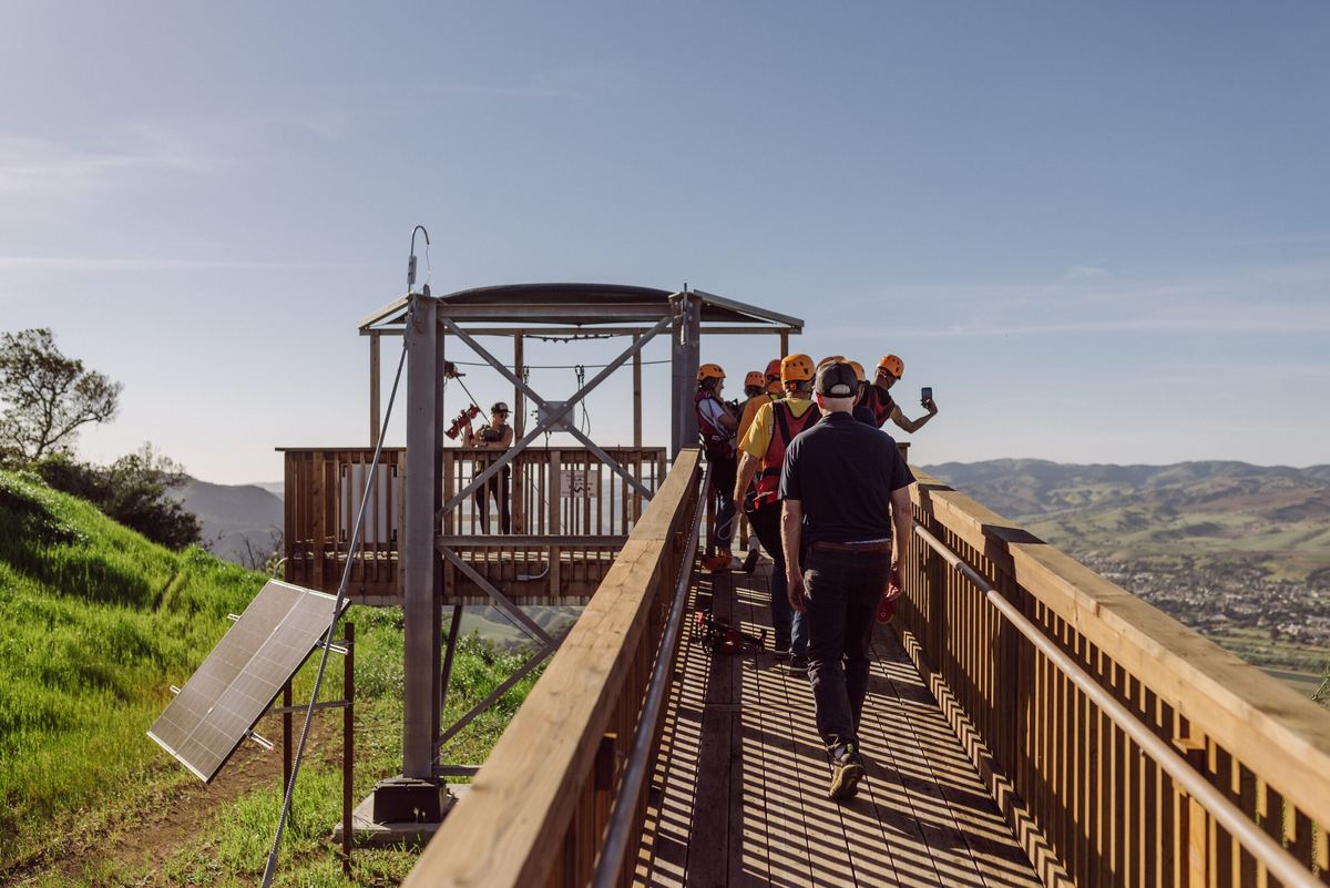 A group in helmets and harnesses walking the platform walkway before their zipline session.