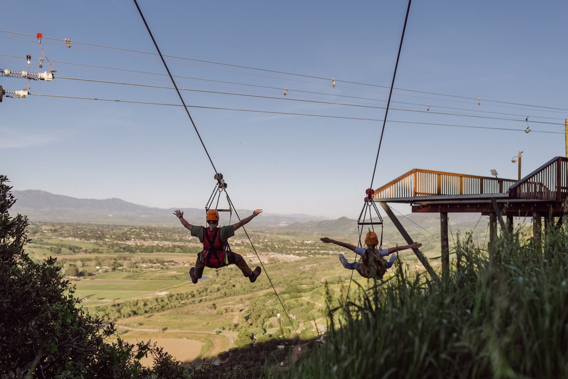 Two colleagues launching side by side from the zipline platform above the Santa Ynez Valley.
