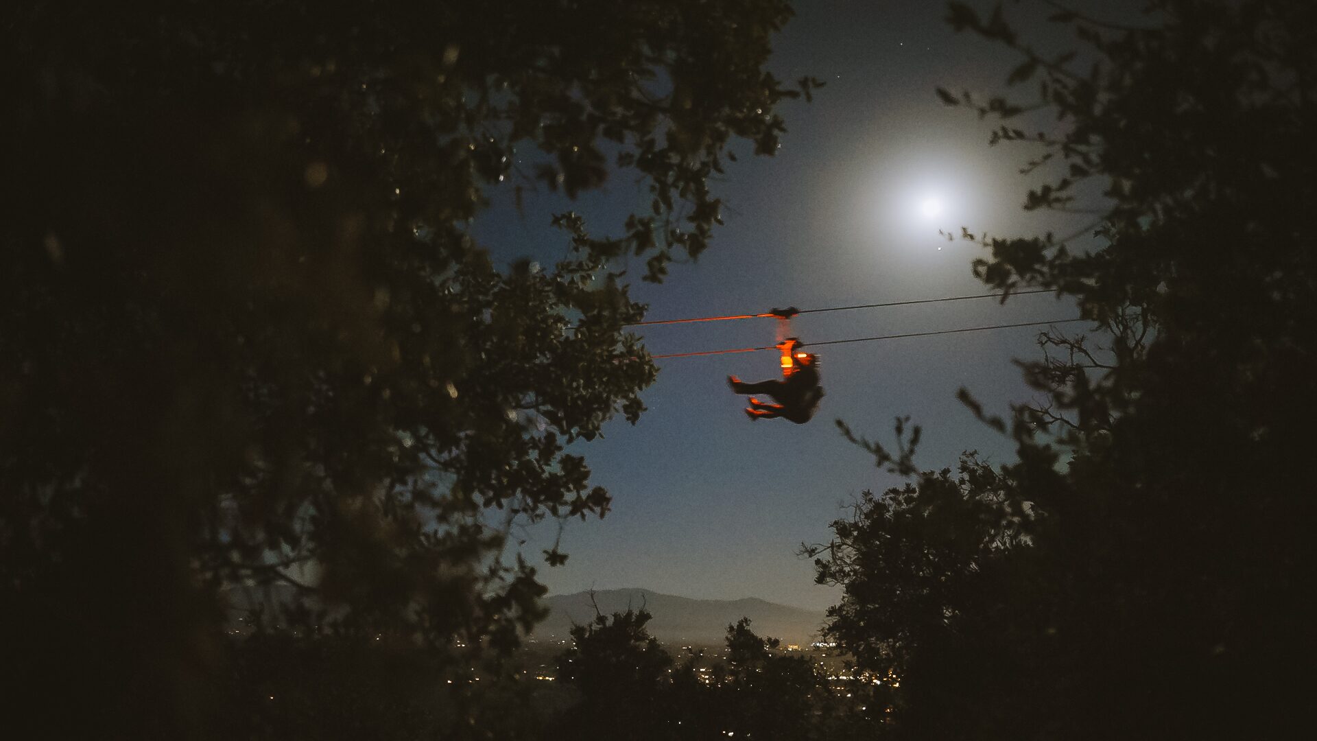 Zipliner flying under the full moon above the oak silhouettes at Highline Adventures, Buellton