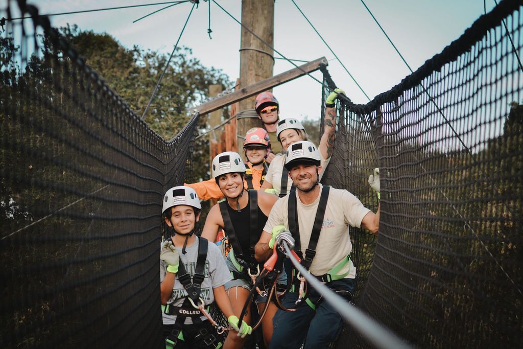 Four friends in helmets and harnesses laughing together on the Adventure Course at Highline Adventures