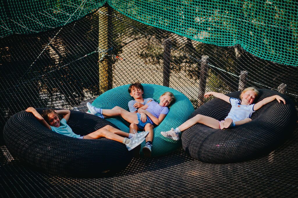 Kids lounging in a net pod of the Skynet Playground — no harness, just the enclosed netting