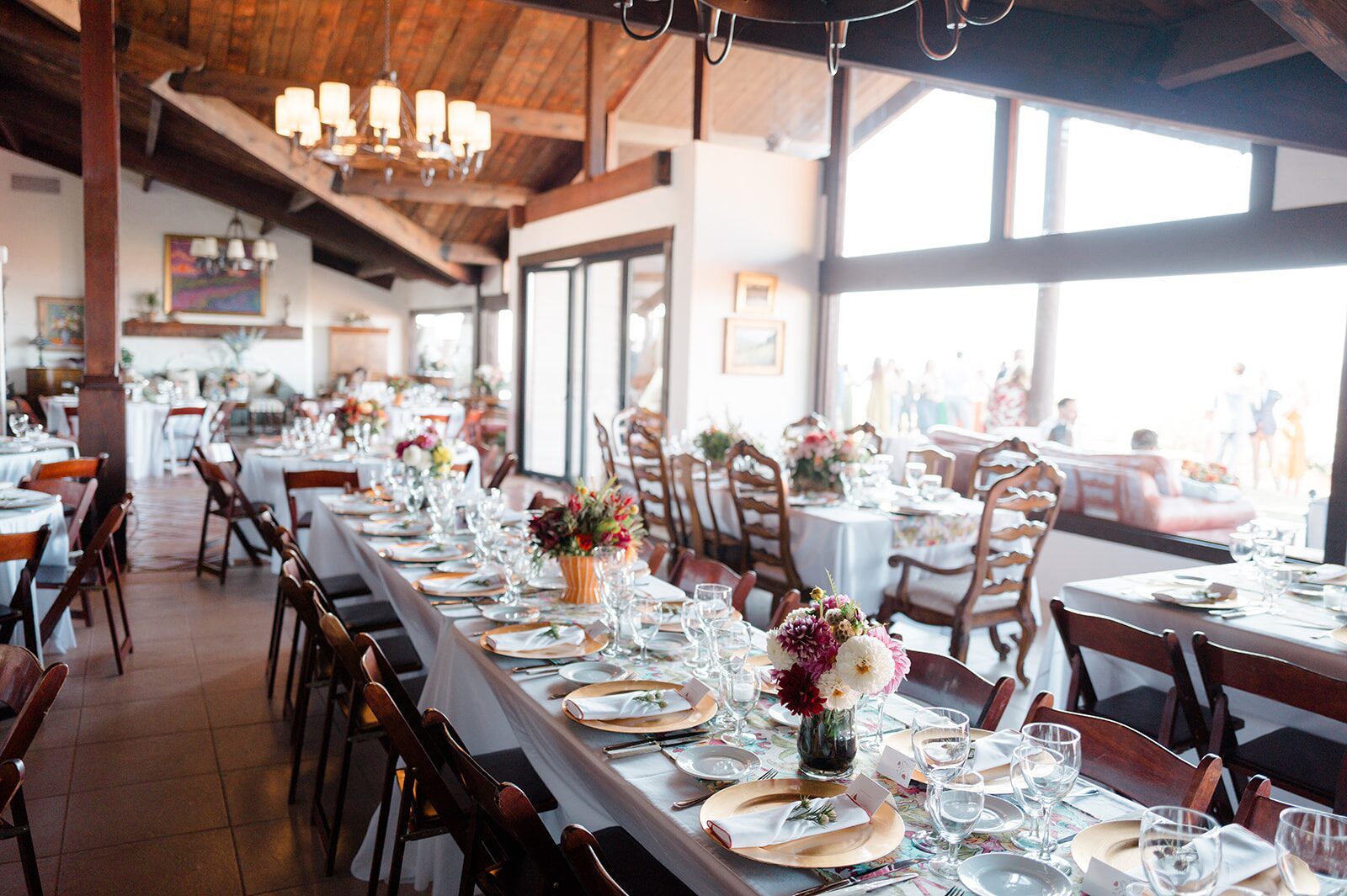 Long dining tables set for a group event inside the Summit House at Highline Adventures, with guests on the terrace beyond