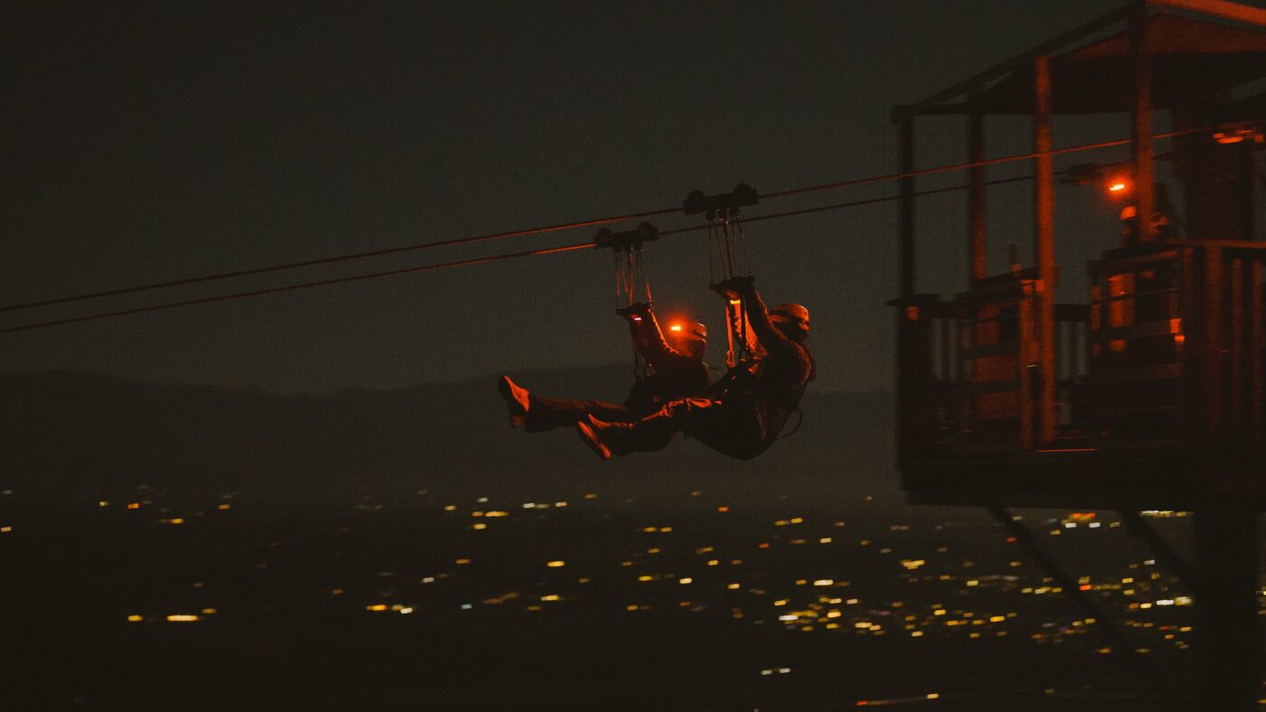 A rider silhouetted against the full moon on the Moonlight Zipline tour, with the valley lights glowing below.