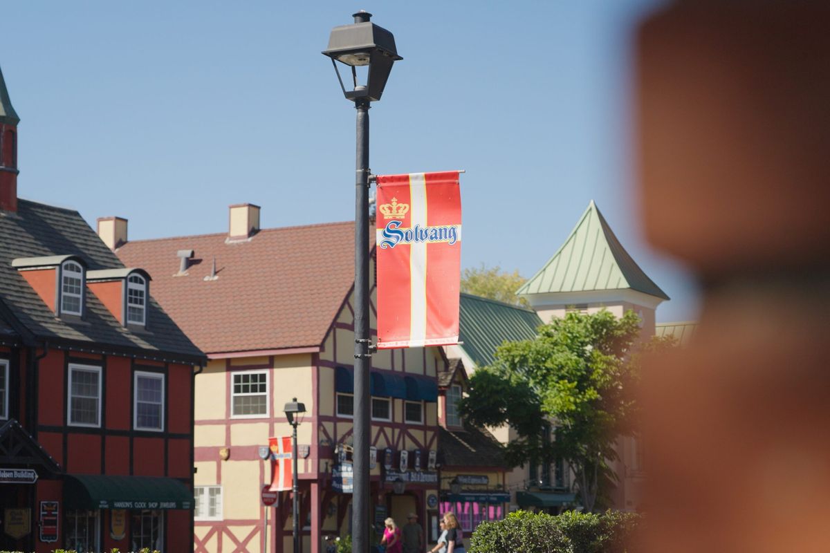A Solvang street with Danish-style storefronts and a red Solvang banner on a lamp post.