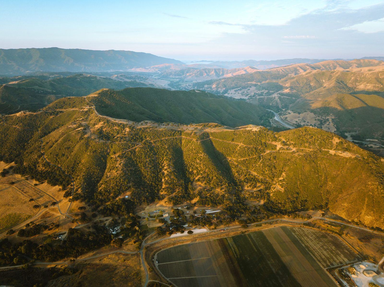 Aerial view of the golden hills of the Santa Ynez Valley at sunset, with ranch land and farm fields below.