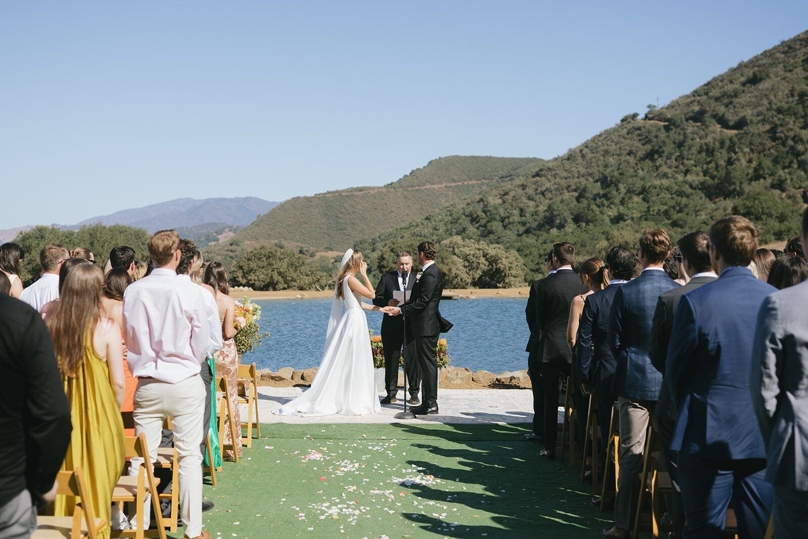Tiffany and Andrew's ceremony on the lakeside lawn, guests seated in rows facing the water.